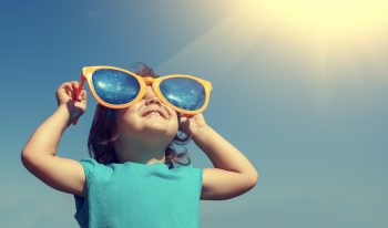 Child looking through oversized plastic glasses toward the sun