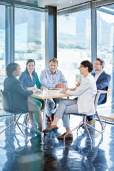 Team, meeting and paper in office for business, marketing strategy and finance management. Corporate people, woman speaker and discussion at table with report, feedback or planning for upcoming audit